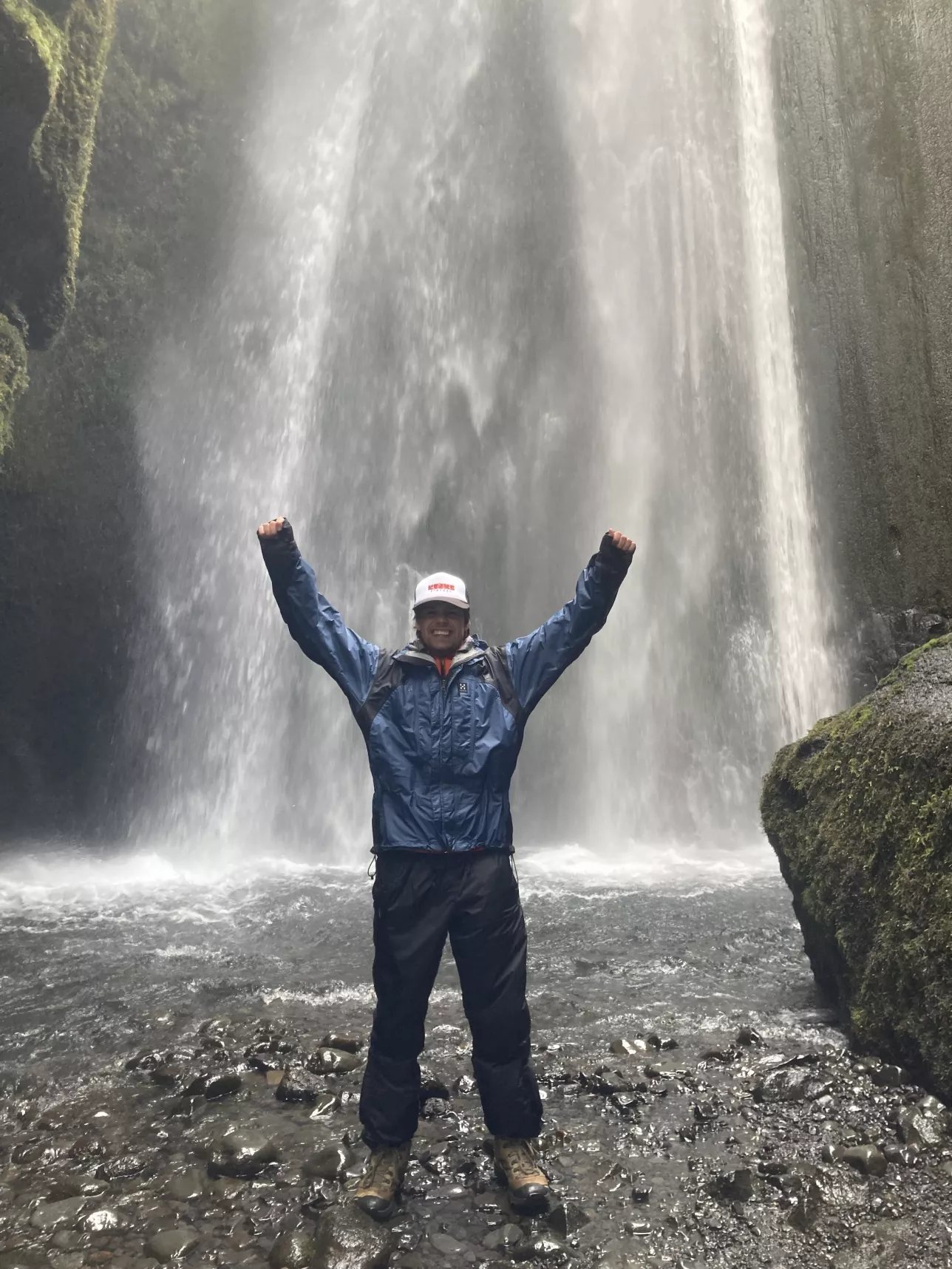 En person står med armarna i luften i bakgrunden syns ett vattenfall.